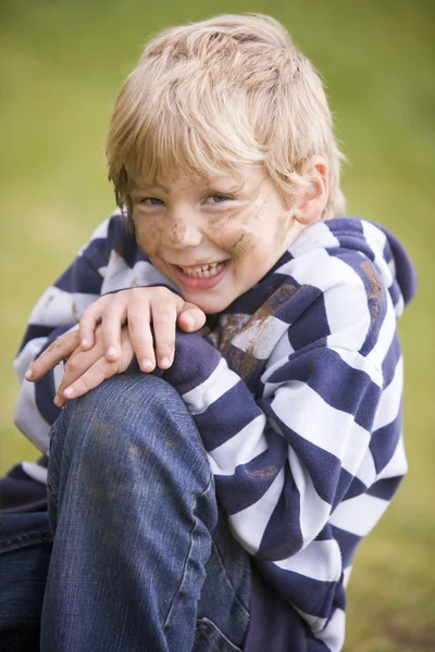 Ung pojke sitter utomhus smutsiga och ler — Stockfoto