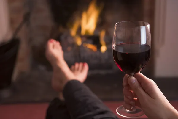 Feet warming at fireplace with hand holding wine — Stock Photo, Image
