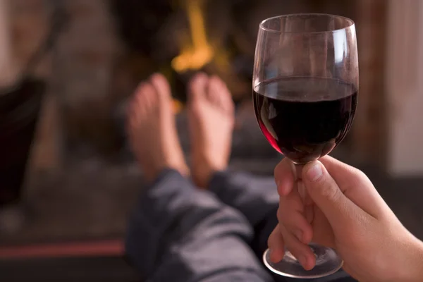 Pés de aquecimento na lareira com mão segurando vinho — Fotografia de Stock