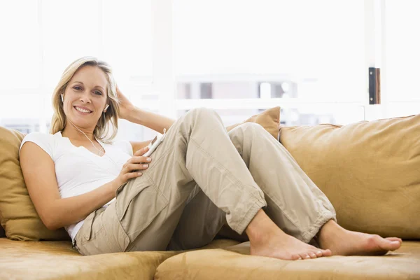 Frau im Wohnzimmer hört dem mp3-Player lächelnd zu — Stockfoto