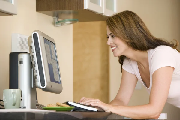Woman in kitchen with computer smiling — Stock Photo, Image