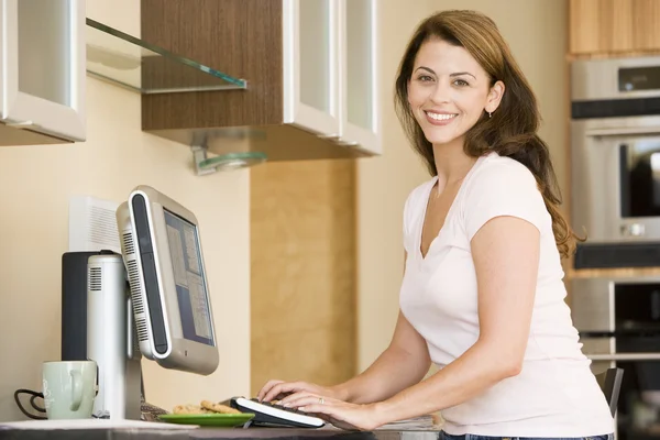 Kadın gülümseyerek bilgisayar ile mutfakta — Stok fotoğraf
