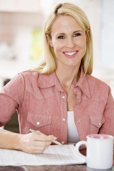 Vrouw in keuken met krant en koffie glimlachen — Stockfoto