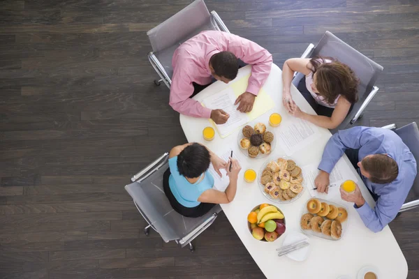 Vier Geschäftsleute am Vorstandstisch mit Frühstück — Stockfoto