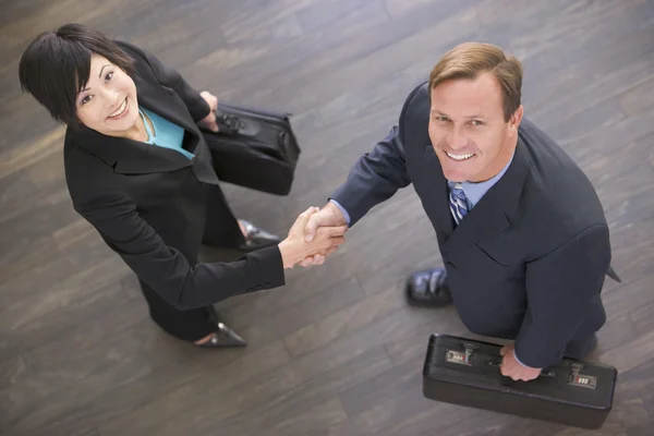 Two businesspeople indoors shaking hands smiling — Stock Photo, Image