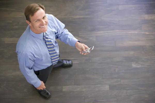 Geschäftsmann steht drinnen und hält lächelnd sein Handy in der Hand — Stockfoto