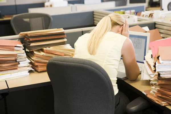 Businesswoman in cubicle with laptop and stacks of files — Stock Photo, Image