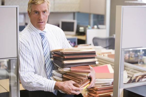 Businessman standing in cubicle holding stacks of files — Stock Photo, Image