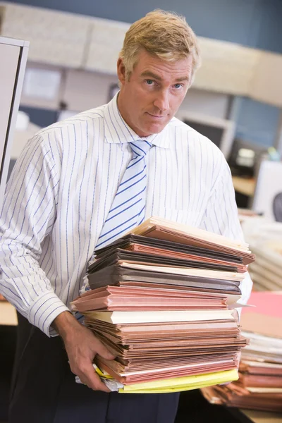 Empresário de pé no cubículo com pilhas de arquivos — Fotografia de Stock