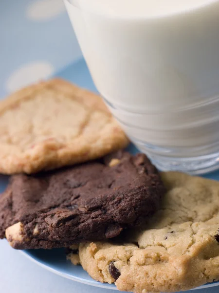 Três biscoitos em uma placa com um copo de leite — Fotografia de Stock