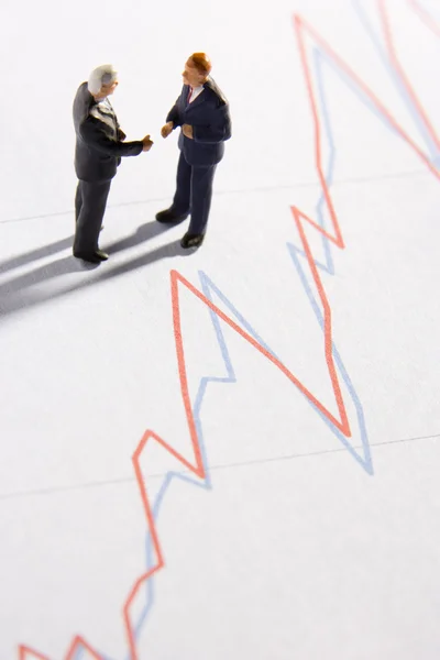 Figuren zweier Geschäftsleute beim Händeschütteln auf einem Liniendiagramm — Stockfoto