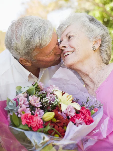 Husband giving wife flowers outdoors kissing and smiling — Stock Photo, Image