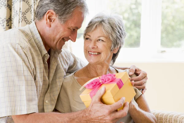 Manžel dává ženě dárek v obýváku s úsměvem — Stock fotografie
