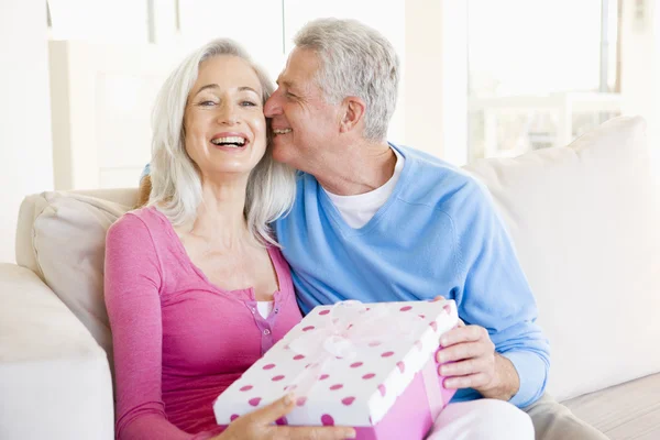 Ehemann schenkt Frau Geschenk im Wohnzimmer, küsst sie und lächelt — Stockfoto