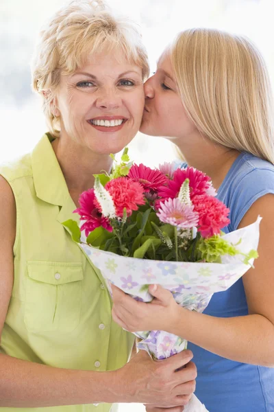 Nieta besando a la abuela en la mejilla sosteniendo flores y s — Foto de Stock