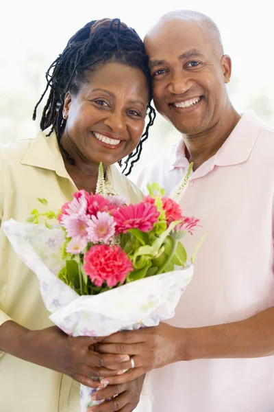 Husband and wife holding flowers smiling — Stock Photo, Image