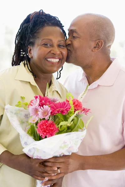 Husband and wife holding flowers kissing and smiling — Stock Photo, Image