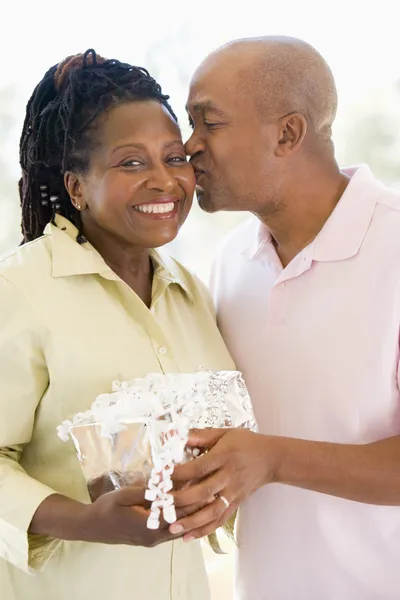 Husband and wife holding gift kissing and smiling
