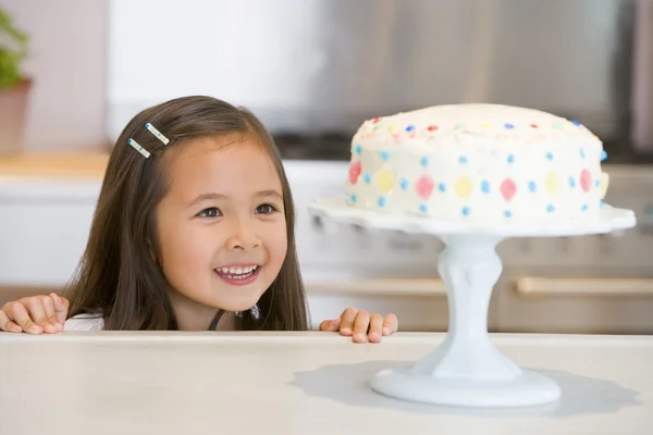 Νεαρό κορίτσι στο μετρητή κουζινών κοιτάζοντας χαμογελώντας κέικ — Φωτογραφία Αρχείου