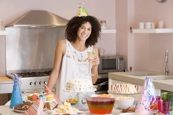 Женщина на вечеринке держит напиток стоя у стола с едой улыбаясь — стоковое фото