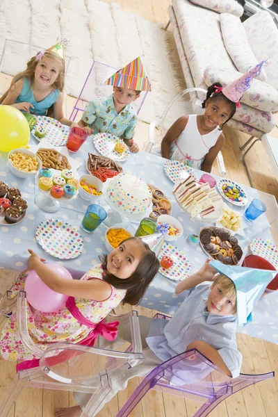 Μικρά παιδιά στο κόμμα που κάθεται σε τραπέζι με χαμογελαστά τροφίμων — Φωτογραφία Αρχείου