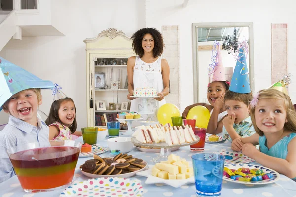 Malé děti na oslavě sedí u stolu s matkou nesoucí ca — Stock fotografie