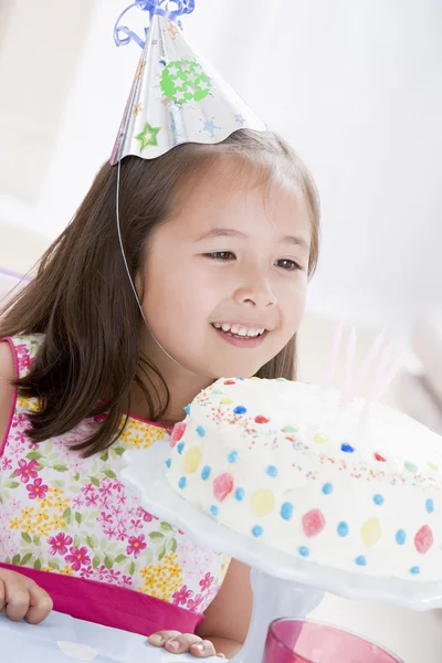 Menina jovem usando chapéu de festa olhando para o bolo de aniversário sorrindo — Fotografia de Stock
