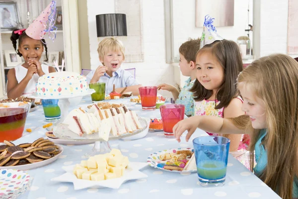 Маленькі діти на вечірці сидять за столом з їжею посміхаючись — стокове фото