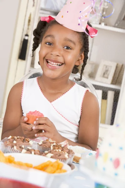 Ung flicka på fest sitter vid bord med en cupcake leende — Stockfoto