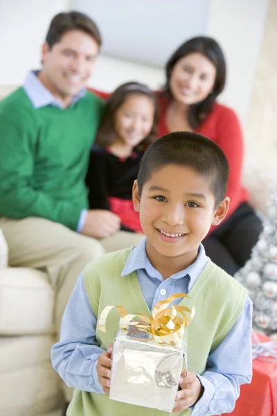 Menino de pé segurando presente de Natal, com seus pais um — Fotografia de Stock