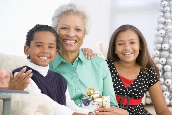 Großmutter sitzt mit ihren beiden Enkeln und hält ein Weihnachtsgeschenk in der Hand — Stockfoto
