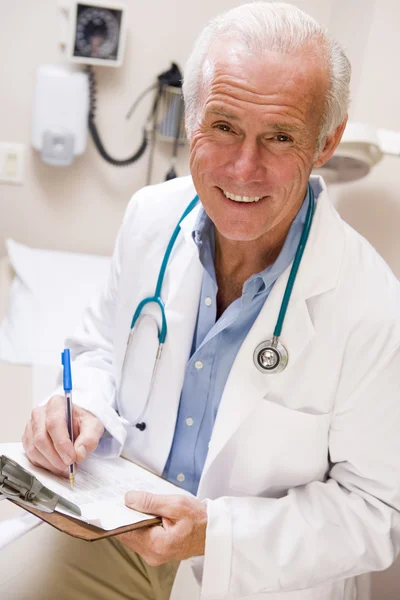 Médico de mediana edad escribiendo en su portapapeles —  Fotos de Stock