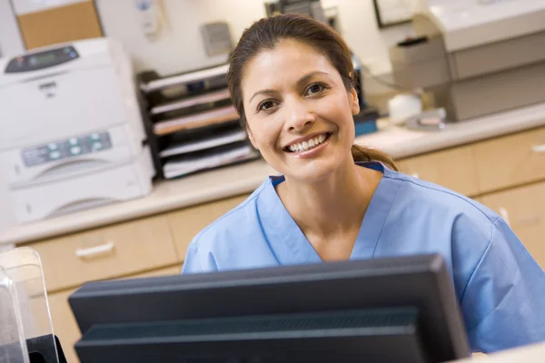 Een verpleegster zit op een computer bij de receptie van een hospita — Stockfoto