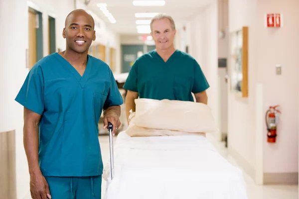 Två sjukvårdare pressar en sjukhuskorridor en tom säng — Stockfoto