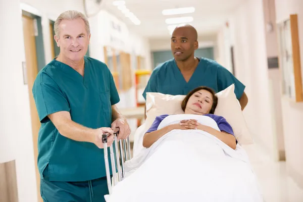 Twee helpers duwen van een vrouw in een bed door een ziekenhuis gang — Stockfoto