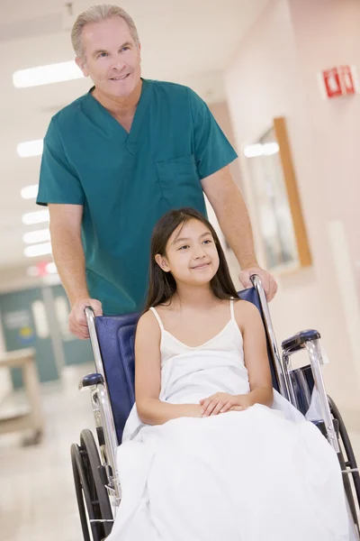En ordnad som driver en liten flicka i rullstol ner ett sjukhus — Stockfoto