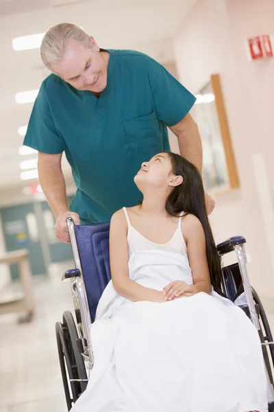 Uma ordenada empurrando uma menina em uma cadeira de rodas para baixo de um hospital — Fotografia de Stock