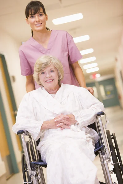 Un'infermiera che spinge una donna anziana su una sedia a rotelle in un ospedale C — Foto Stock