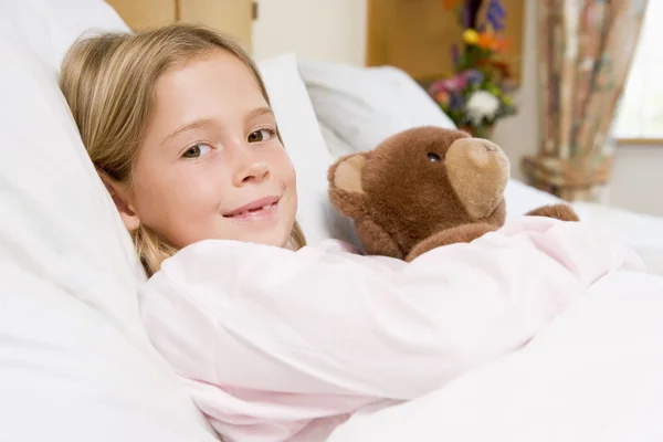 Jovem deitada na cama do hospital, segurando ursinho de pelúcia — Fotografia de Stock