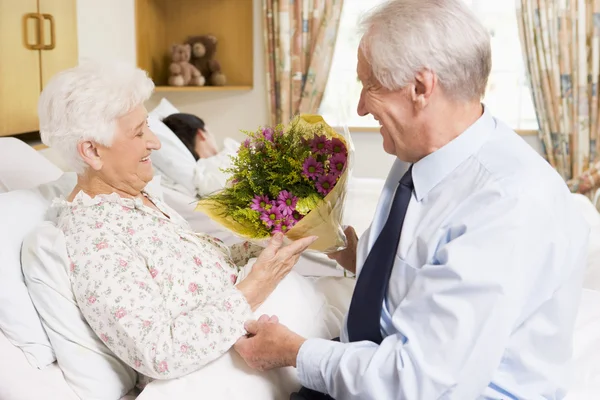 Senior man die bloemen geeft aan zijn vrouw in het ziekenhuis — Stockfoto