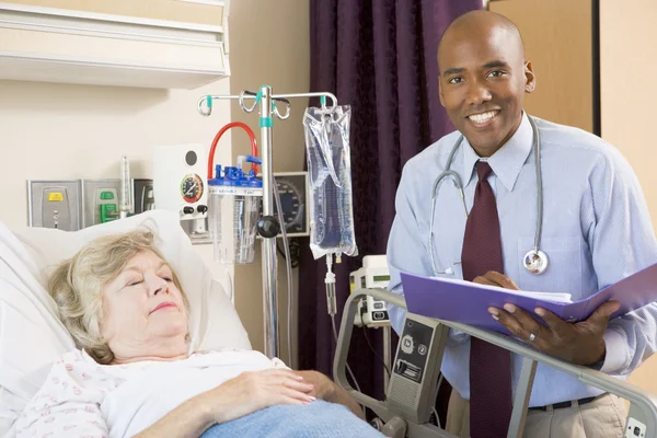 Medico prendendo appunti su anziano donna sdraiata in ospedale letto — Foto Stock