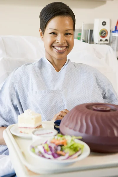 Femme assise dans un lit d'hôpital avec un plateau de nourriture — Photo