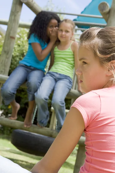 Дві подруги молодої дівчини на дитячому майданчику шепочуться про інший гіт — стокове фото