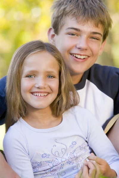 Bror och syster sitter utomhus leende — Stockfoto
