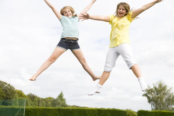 Two young girls jumping on trampoline smiling — Stock Photo, Image
