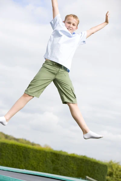 Мальчик прыгает на батуте улыбаясь — стоковое фото