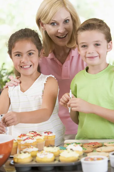 Woman with two children in kitchen decorating cookies smiling Stock Image