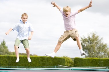 Two young boys jumping on trampoline smiling clipart