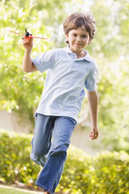 Young boy with toy airplane running outdoors smiling clipart