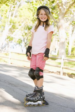 Young girl outdoors on inline skates smiling clipart